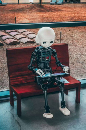 A white robot sitting on a red bench, looking at a tablet.