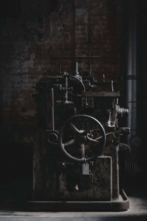 Close-up of an old, rusty industrial machine with pipes and a large wheel.