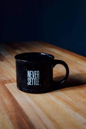 Black coffee mug with the words 'Never Settle' on a wooden surface
