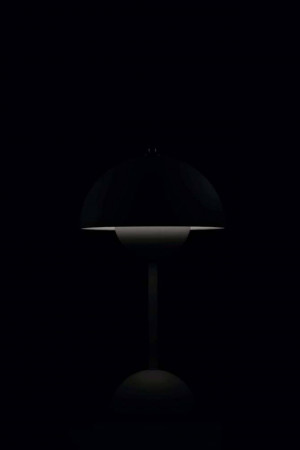 A dark image of a modern table lamp with a round shade.