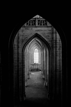 Black and white photograph of a gothic archway leading to a bright window.
