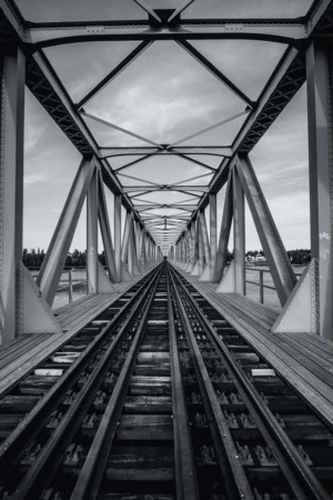 Black and white photograph of a steel truss bridge with converging railway tracks.