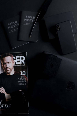 Black notebook, pen, phone, magazine and wallet on a dark surface