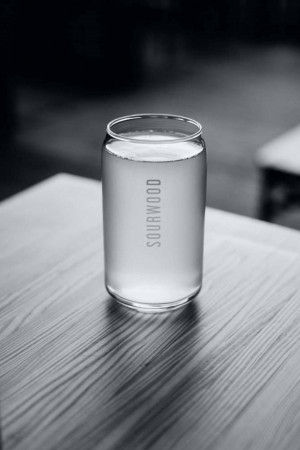 A black and white image of a tall, slim can of Sourwood beverage on a wooden surface.
