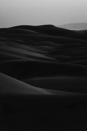 Black and white image of rolling sand dunes in a desert landscape.
