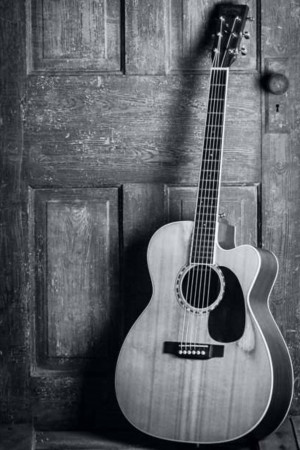 Black and white image of an acoustic guitar leaning against a rustic wooden door.