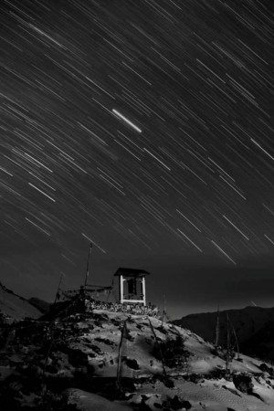 Long exposure photograph of star trails over a small shrine on a mountain peak.