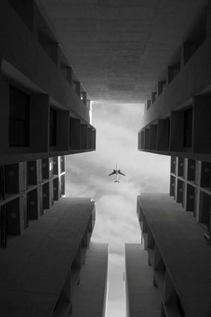 Airplane flying through a gap between concrete buildings