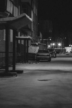 Black and white image of cars parked on a snowy street at night.