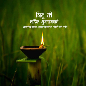 A lit diya lamp in a field, with text wishing a happy Bihu.