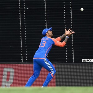 Indian cricketer in blue jersey stretching to catch a cricket ball during a match.