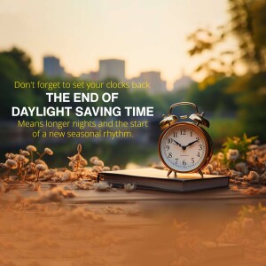 Alarm clock on a book with a blurred city and autumn foliage background, reminding people to set their clocks back.