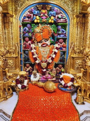 Close-up of a vibrant Hanuman idol adorned with flowers and garlands within a richly decorated temple.