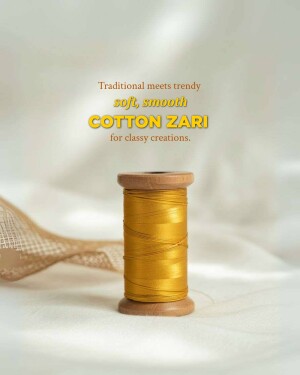 Close-up of a wooden spool of golden cotton zari thread with fabric in the background.