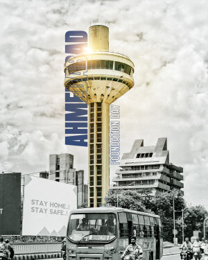 A tall tower with 'Ahmedabad Foundation Day' text against a cloudy sky and cityscape.