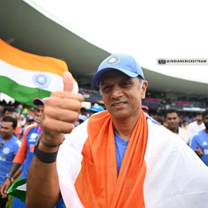 Rahul Dravid, the coach of the Indian Cricket Team, giving a thumbs up with the team in the background.