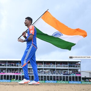 Indian cricketer walking with the Indian flag on the field